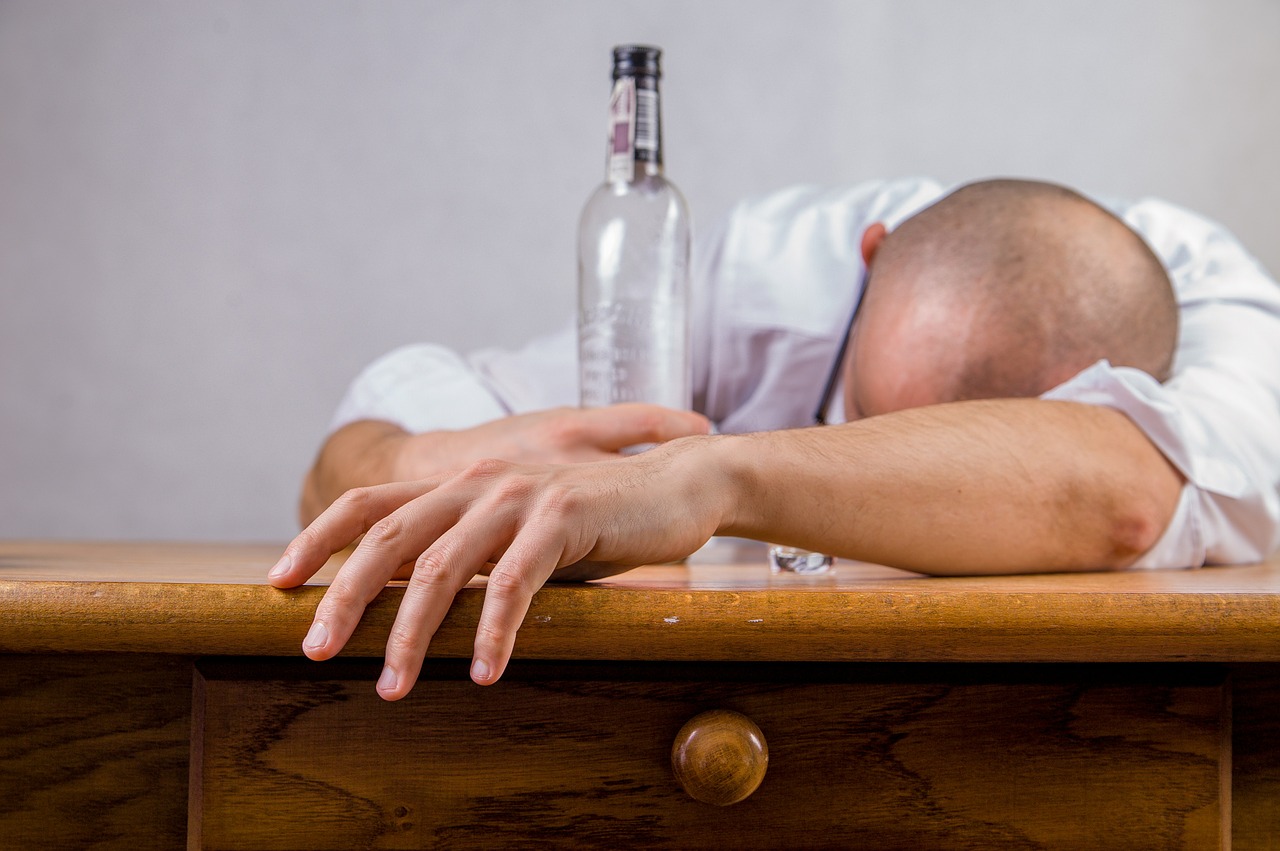 man hungover a wooden desk holding onto an empty bottle